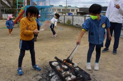 たき火の中の木を火箸で動かしたり、うちわで扇いだりしている写真