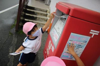 3歳児が背伸びをしてハガキをポストに投函している写真