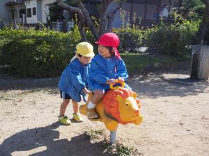 ロッキング遊具で遊ぶ3歳児を押してあげている4歳児