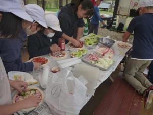 野外炊飯でピザ生地に野菜をのせている様子