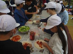 野外炊飯でピザ生地にピザソースをぬっている様子