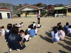 避難訓練で幼児が園庭に避難し園長先生のお話を聞いている写真