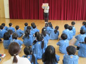  遊戯室で幼児がひな祭りについての紙芝居を見ている写真