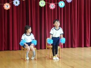 男の子前に立ち、その横で女の子が座っている写真