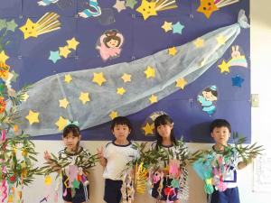七夕の掲示物の前で笹をもってポーズを決める子ども達の写真