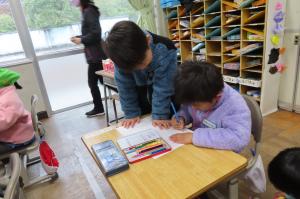 小学校の教室に入り、椅子に座って絵を描いているところ