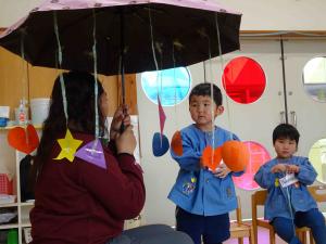 様々な形がぶら下がっている傘を持っている先生の写真