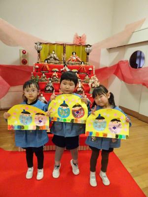 雛人形の前で、自分たちが作った雛飾りを持っている写真