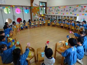 全園児が丸く座り、コップを持っている写真